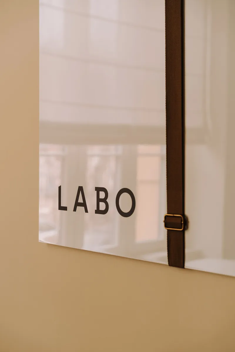 Interior glass partition with leather strap detail and text lettering viewed from a pale yellow wall