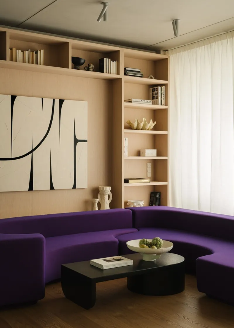Built-in plywood shelving with books and objects above a purple curved sectional sofa