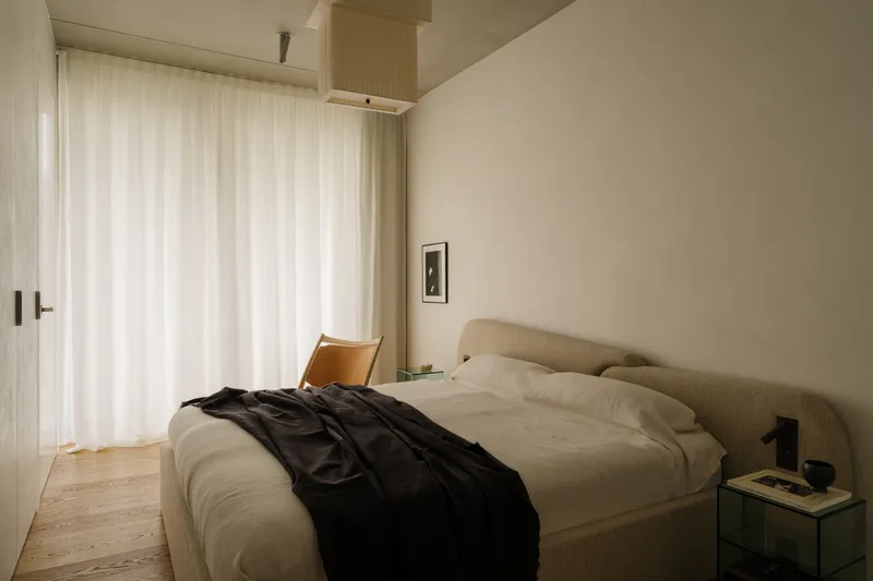 Bedroom with upholstered bed and timber column beneath a vaulted ceiling with soft daylight through sheer curtains