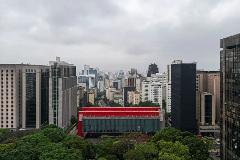 Elevated view of the red-framed glass bridge connecting buildings amid the dense high-rise cityscape and tree canopy