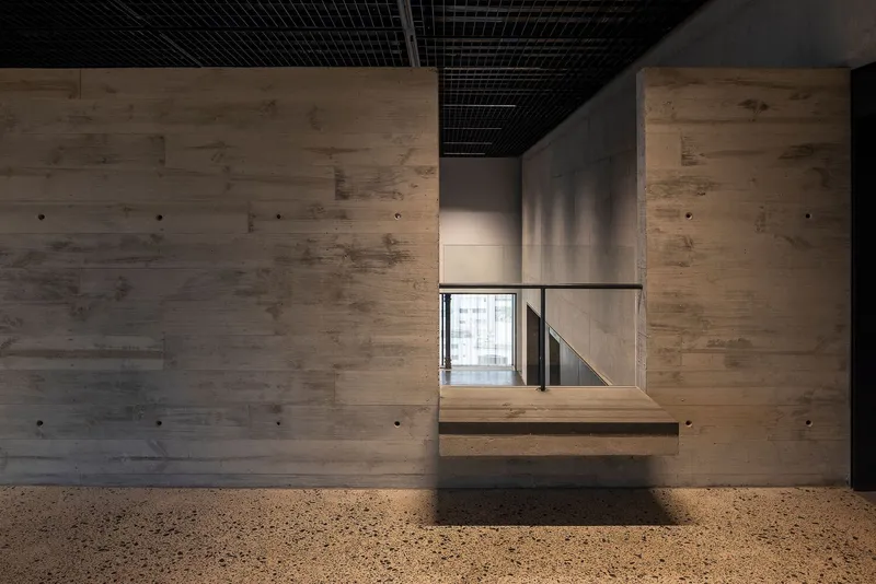 Cantilevered timber bench below a board-formed concrete opening framing a window beyond