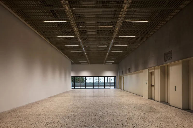 Gallery space with terrazzo floor, metal mesh ceiling and linear light strips above white walls