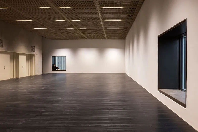Dark timber floor stretching toward corner window with figure seated inside the aperture