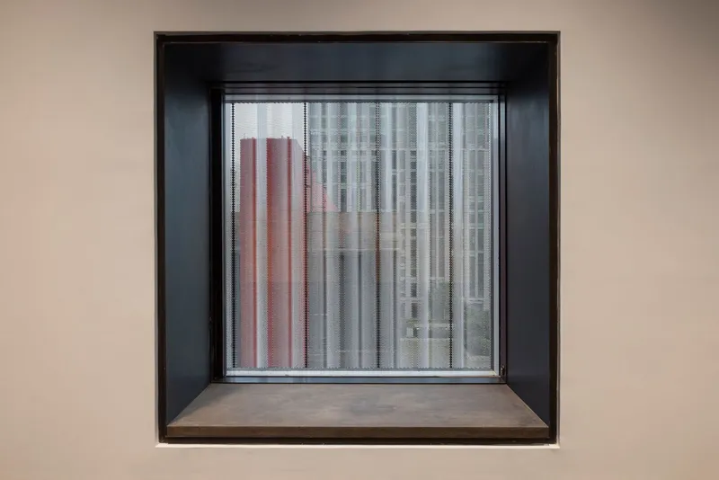 Deep-set window with black steel frame and timber sill framing a view of neighboring towers
