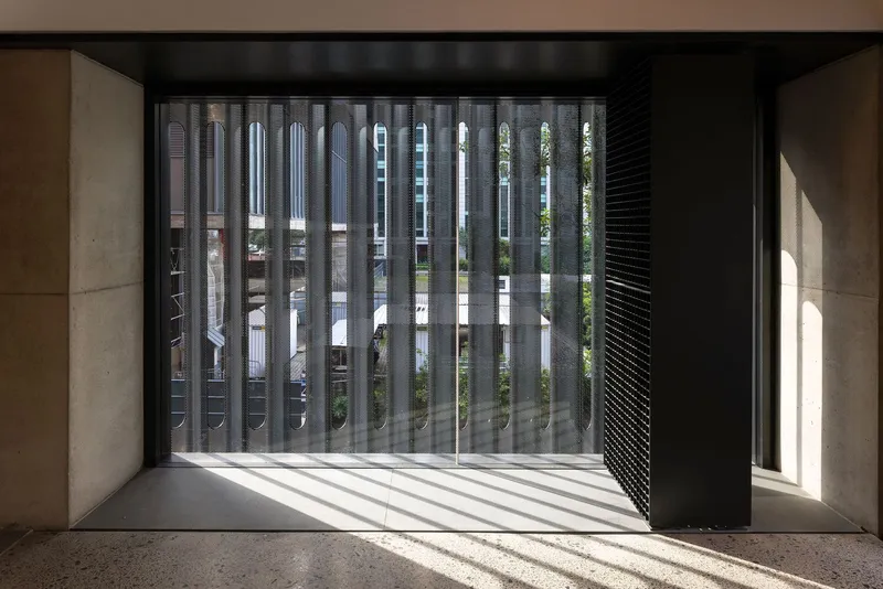 Interior balcony with vertical metal screen filtering afternoon sunlight into striped shadows on concrete floor