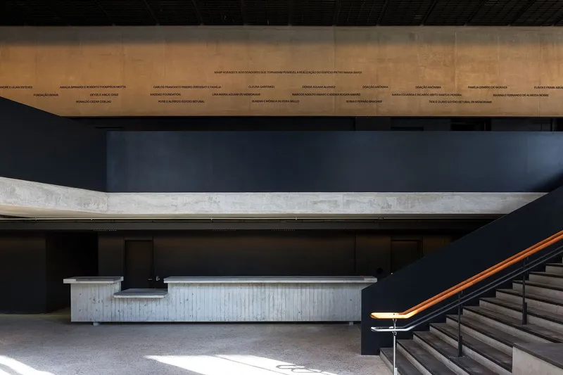 Interior lobby with concrete service desk and bronze-railed staircase in afternoon sunlight