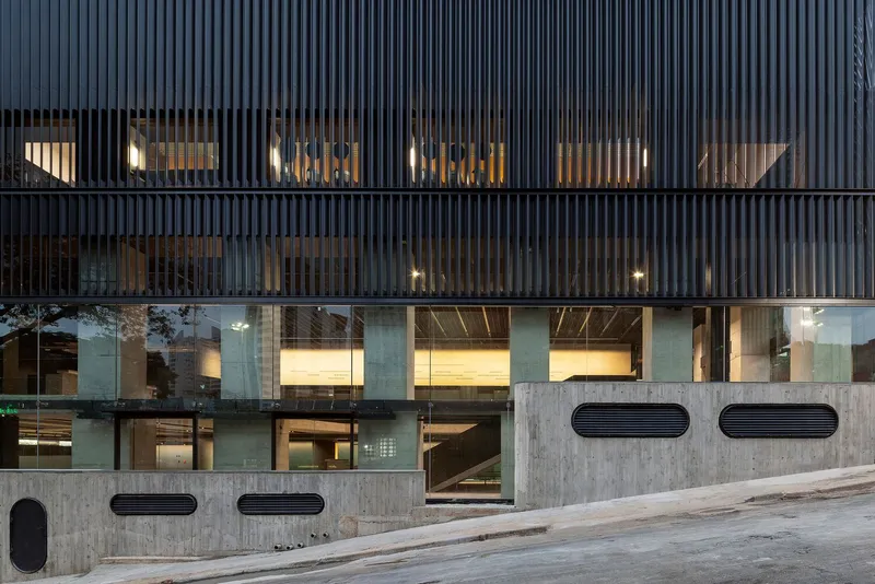 Facade with vertical metal fins over glazing and exposed concrete base at dusk