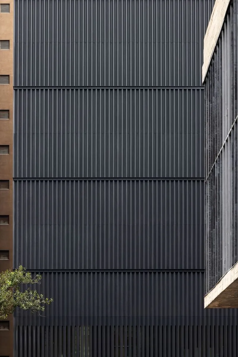 Close-up of the corrugated metal cladding with horizontal panel joints and neighboring foliage