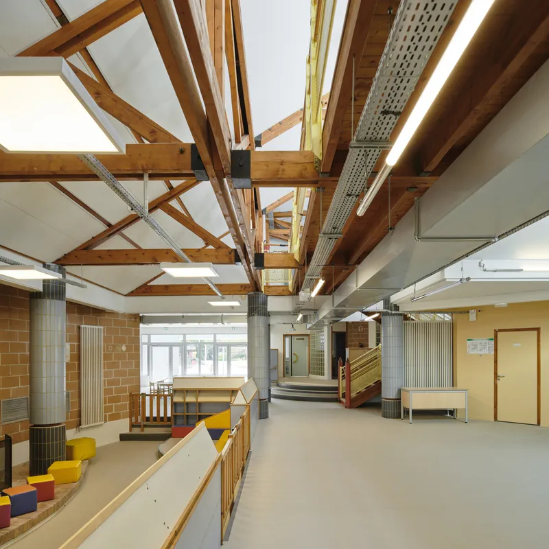 Exposed timber roof structure with steel connectors and perforated acoustic panels above a circulation space