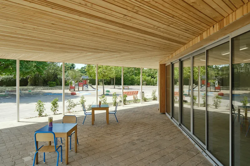 Covered terrace with slatted timber ceiling, white columns and paver floor overlooking a playground with young trees