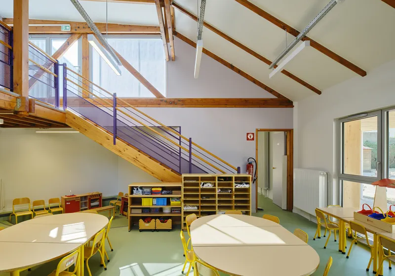 Double-height classroom with timber staircase, exposed roof trusses and sunlight streaming through high clerestory windows