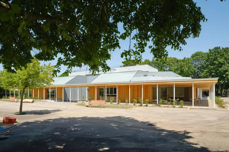 Single-story timber-clad structure with wraparound veranda and corrugated metal roof beneath leafy trees