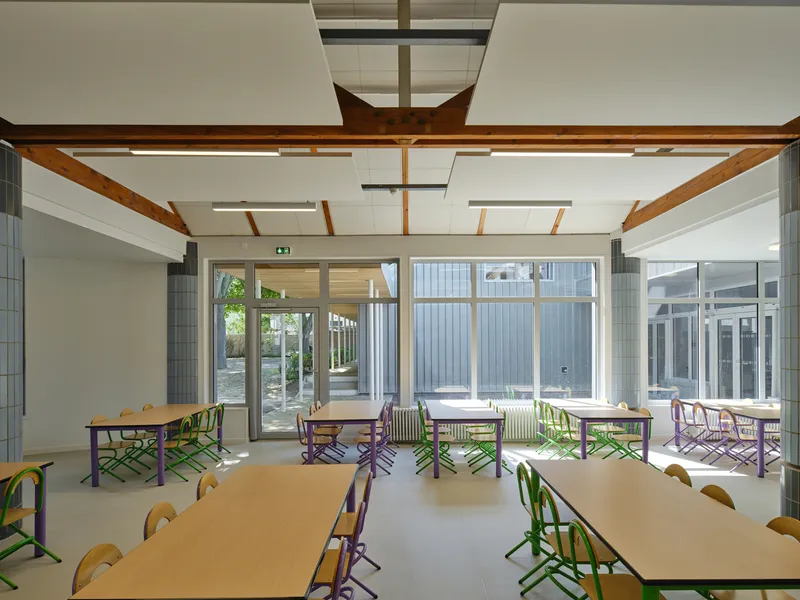Dining hall with exposed timber beams and colorful chairs arranged at long tables beneath skylights