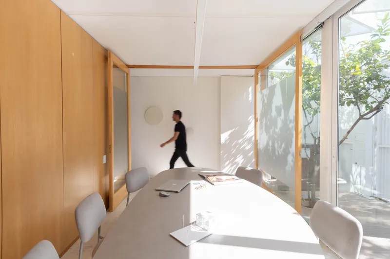 White meeting room with sliding timber-framed partitions and dappled sunlight from the courtyard