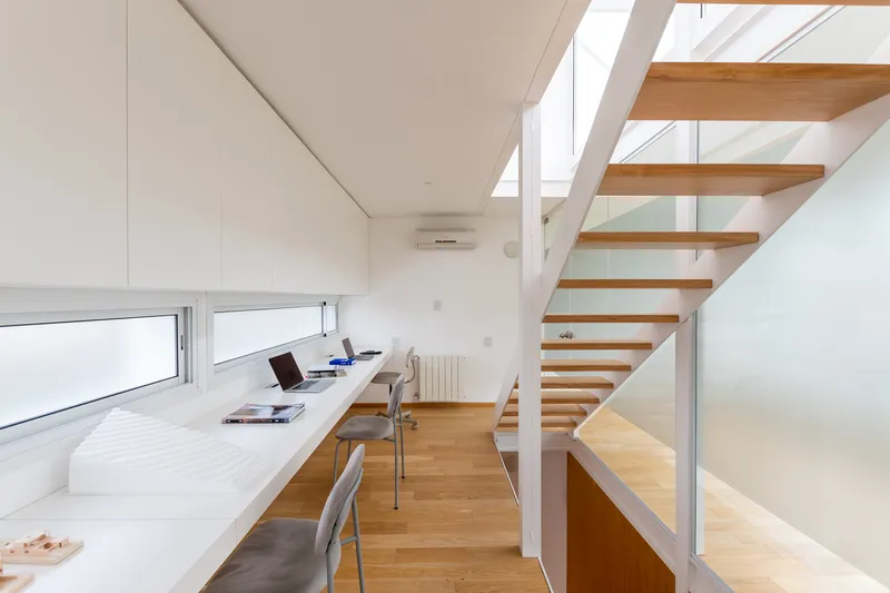 Open-tread timber staircase ascending beside a white worktop beneath a high clerestory window