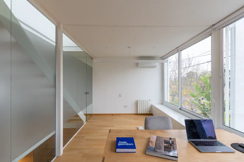 Light-filled desk area with corner windows overlooking garden foliage and an open timber staircase beyond