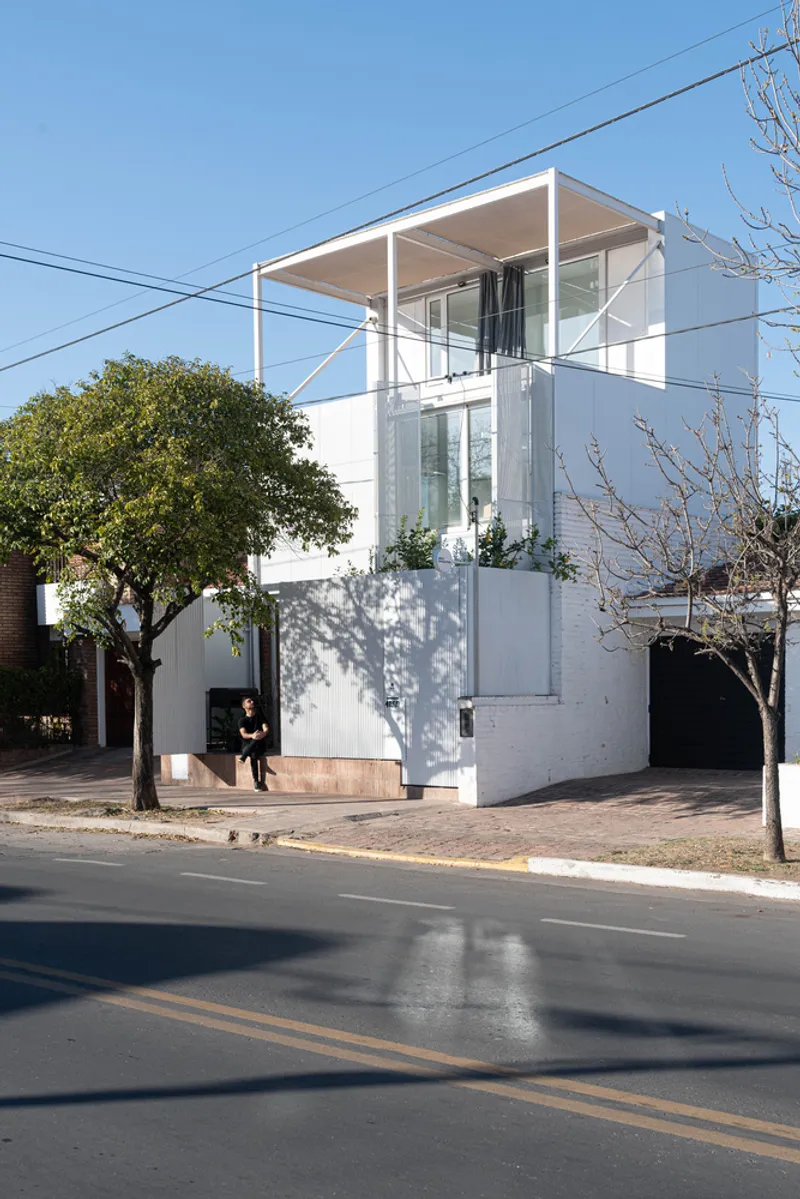Street view of the white stucco facade with rooftop terrace and glass volume flanked by mature trees