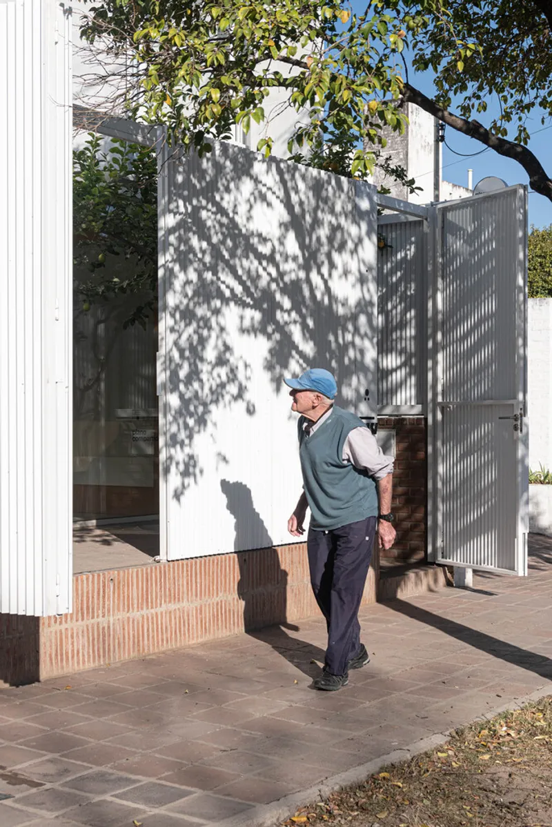 Man walking through the entry courtyard with white corrugated walls casting dappled shadows from overhead branches