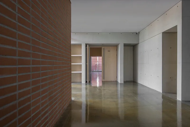 Interior hallway with polished concrete floor reflecting light from distant doorway and exposed brick wall