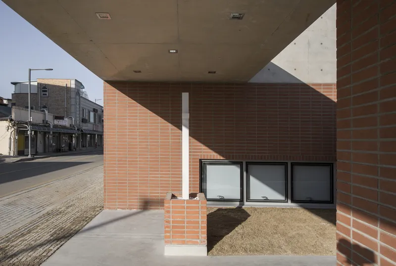 View under the cantilevered concrete soffit showing brick walls and planted bed in shadow