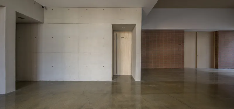 Interior corridor with board-formed concrete walls and polished concrete floors leading to a timber screen