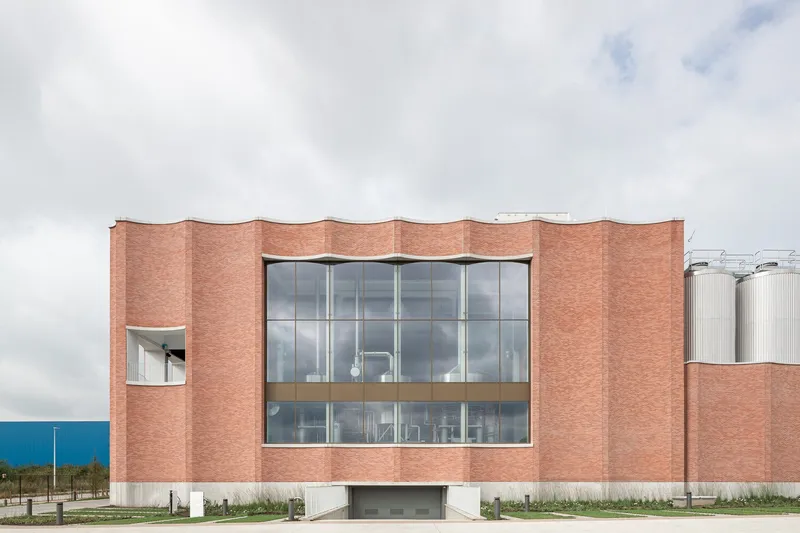 Front elevation of the undulating red brick facade with a central glazed opening under overcast skies