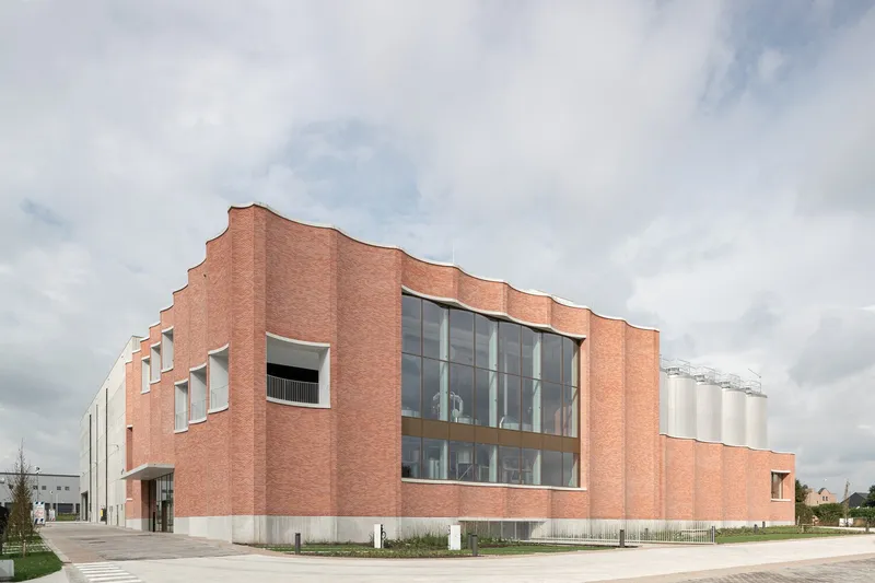 Corner view showing the rhythmic brick folds wrapping the glass-fronted industrial facility