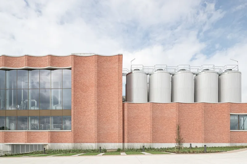 Side elevation showing the corrugated brick walls alongside metallic silos in afternoon light