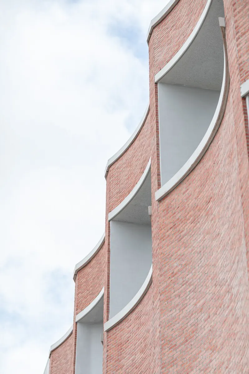 Red brick facade with curved white-edged balconies stacked vertically against an overcast sky