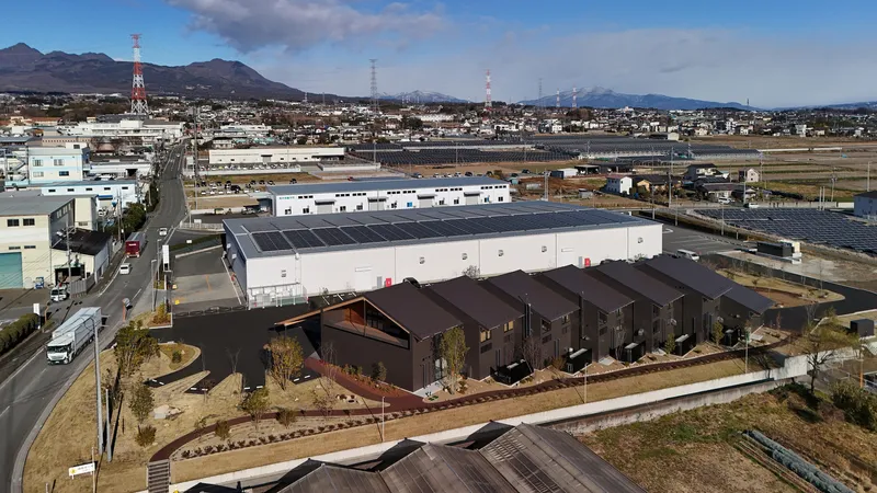 Drone view showing the complex with sawtooth roofs adjacent to farmland and a solar-paneled warehouse building