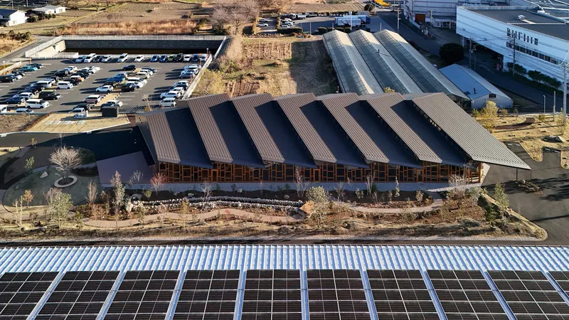 Aerial view of the sawtooth roof structure with dark corrugated metal panels above a planted landscape