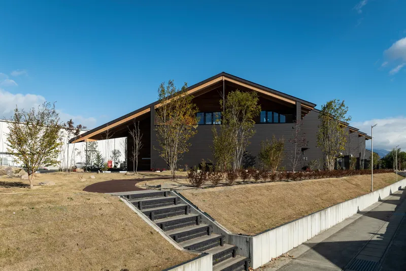 Planted berm with zigzag pathway and concrete steps leading to the dark-clad building facade