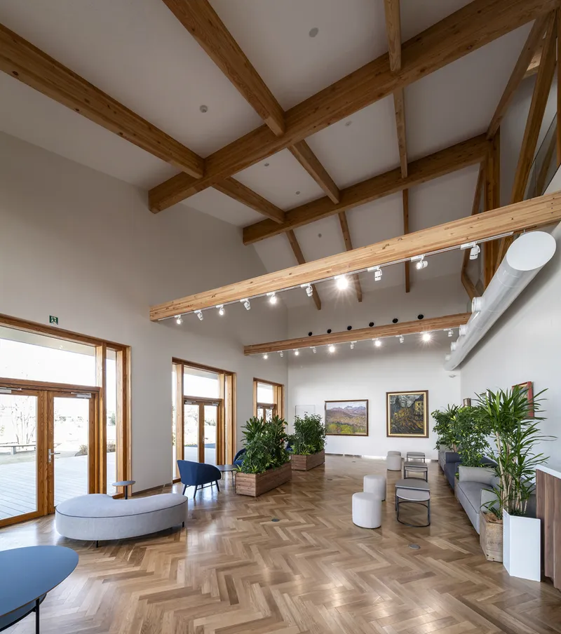 Gallery space with exposed timber beams and track lighting above herringbone wood flooring