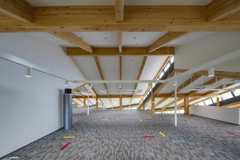 Upper floor corridor with exposed timber rafters, grey carpet tiles marked with colored tape and track lighting