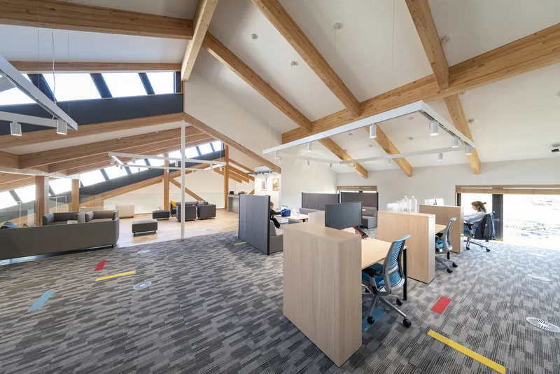 Office workstations beneath timber trusses with a person seated at a desk in daylight