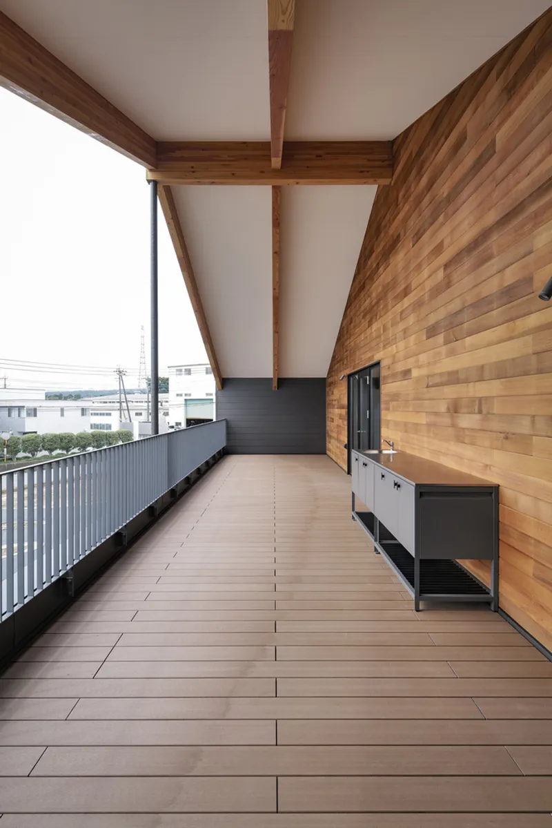 Covered terrace with timber plank wall and diagonal steel bracing overlooking neighboring buildings