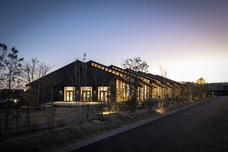 Long view of the illuminated timber-framed building with planted courtyard at twilight