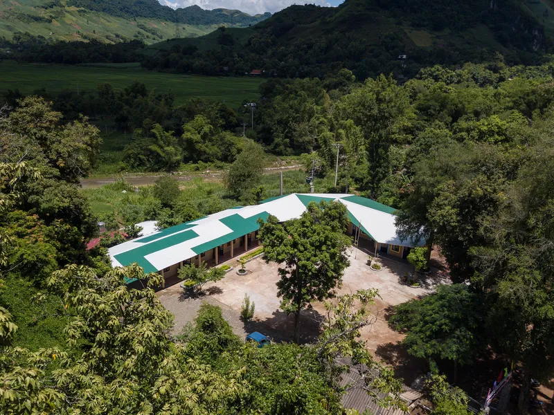 Aerial view of a three-winged structure with green and white roof panels surrounding a central courtyard with trees