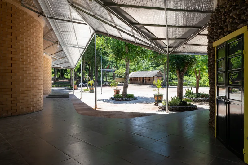 Covered walkway with woven ceiling panels and curved woven brick wall opening to a planted courtyard beyond