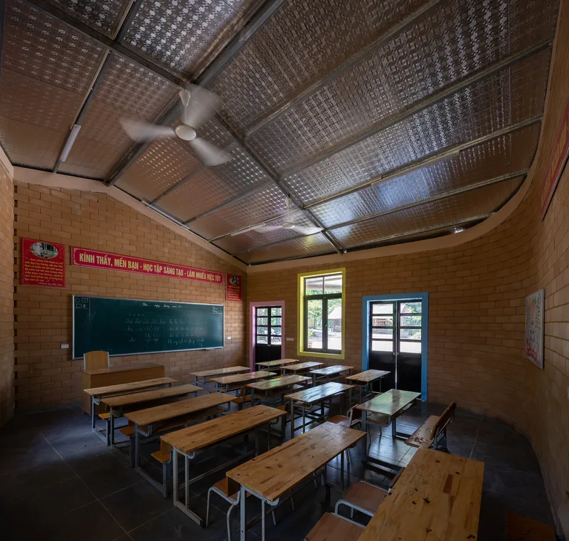 Classroom interior with exposed brick walls, wooden desks, ceiling fan and perforated translucent ceiling panels