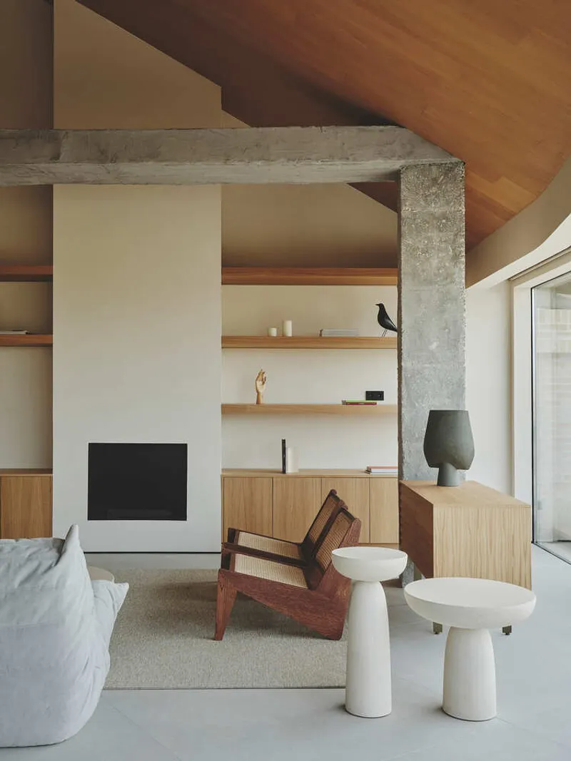Exposed concrete beam spanning above fireplace with timber shelving and curved timber ceiling beyond