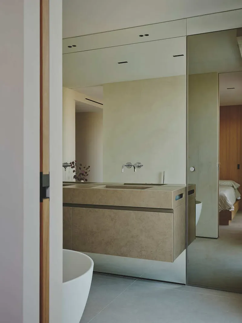 Bathroom vanity with stone-effect floating cabinet, wall-mounted taps, and full-height mirror reflecting bedroom beyond
