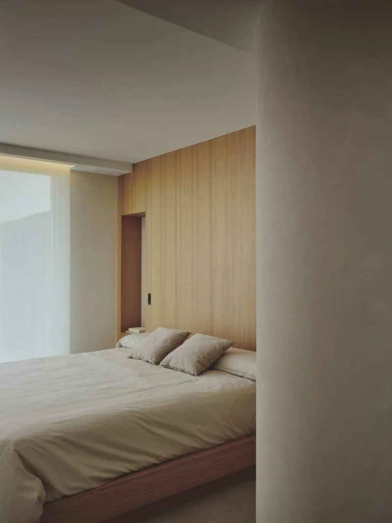 Bedroom with timber-clad headboard wall, low platform bed, and curved white partition at threshold