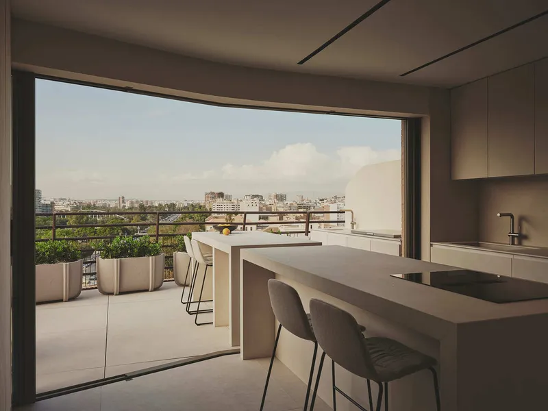 Kitchen island opening to planted terrace with city skyline visible under afternoon clouds