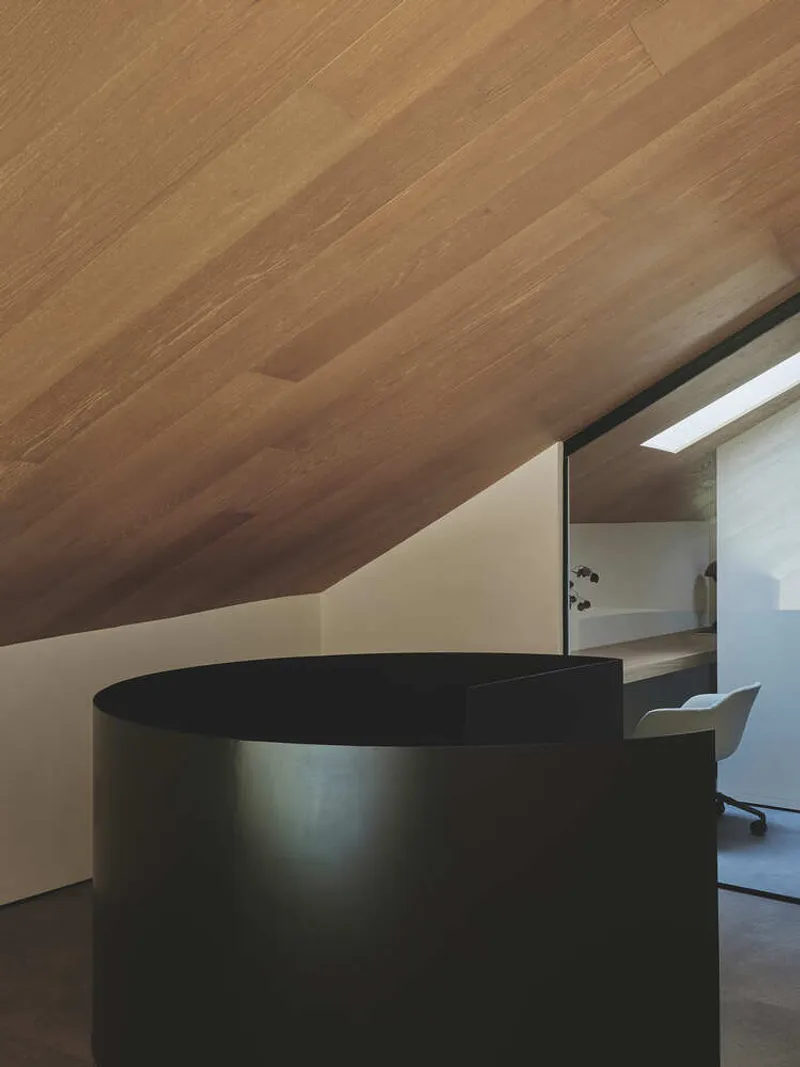 Upper level workspace with curved black reception desk beneath timber-clad sloping ceiling