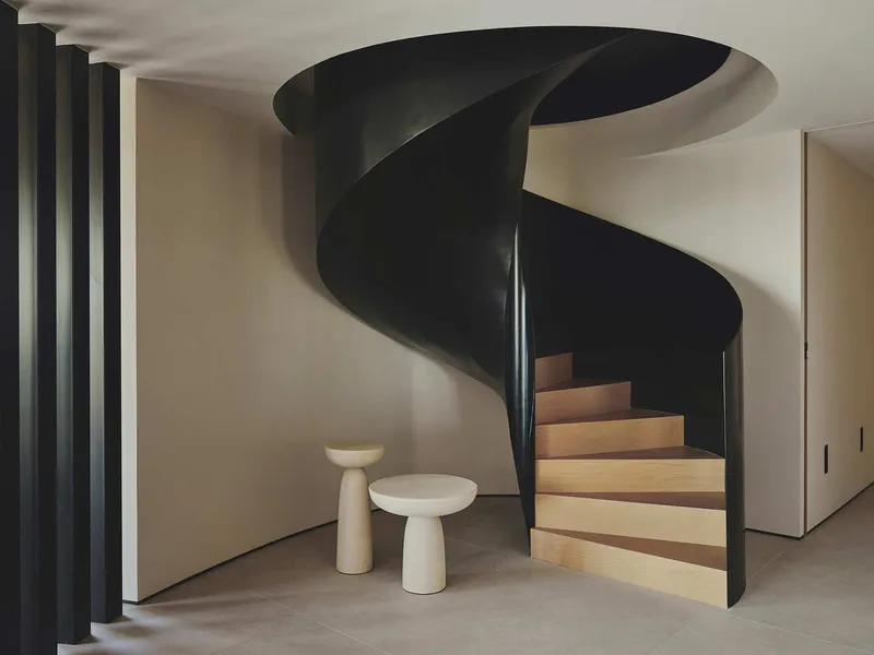 Spiral staircase with black steel undersides and oak treads beside two white stone stools