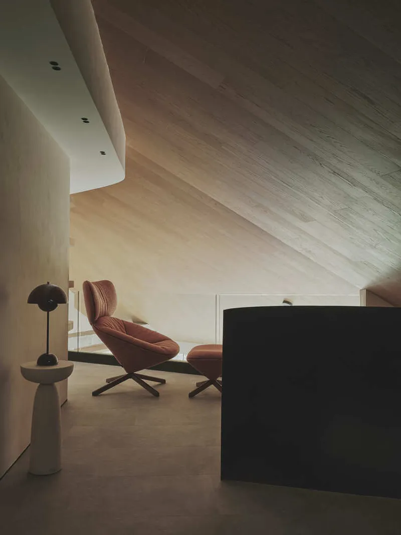 Interior room with angled wood ceiling panels, a terracotta lounge chair, and soft natural light