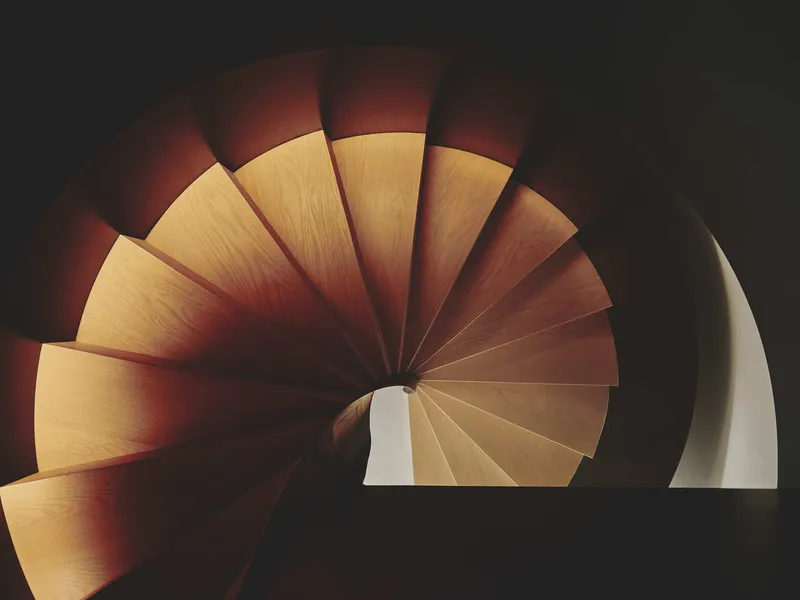 Top-down view of a spiral staircase with wooden treads radiating from a central core in low light