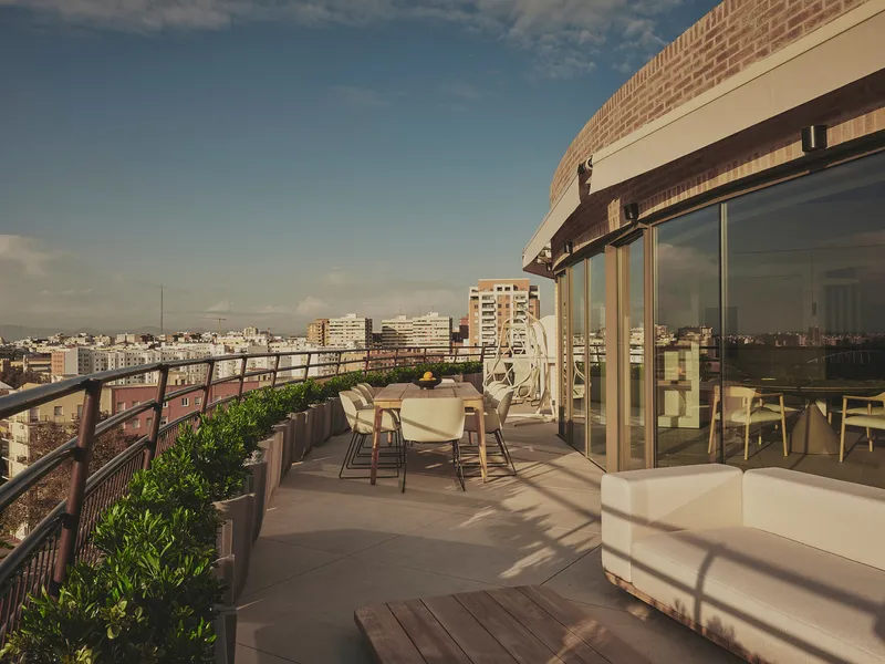 Rooftop terrace with dining table, planted beds, and curved brick parapet at sunset