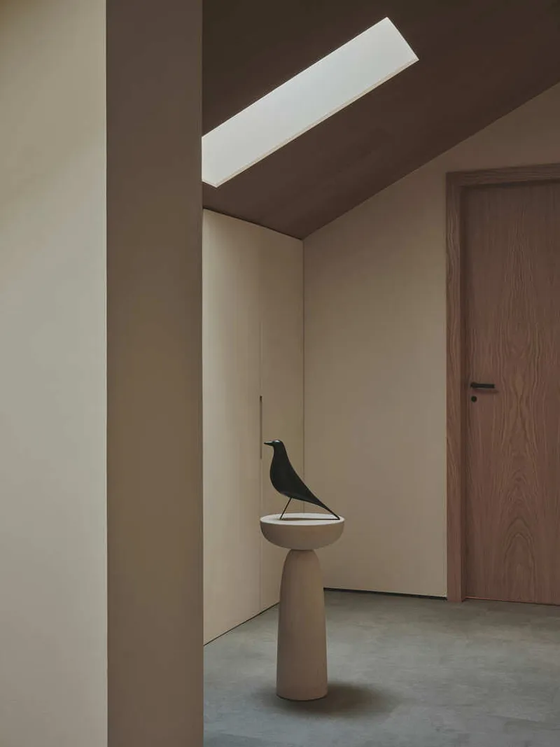 Entry hall with sculptural pedestal and bird object beneath a linear skylight